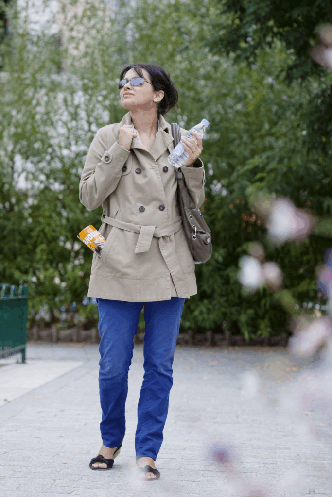 A woman is happily walking through a park while wearing a hip-length canvas coat, confident that she doesn't have to worry about online threats thanks to PhantomMode on her phone.