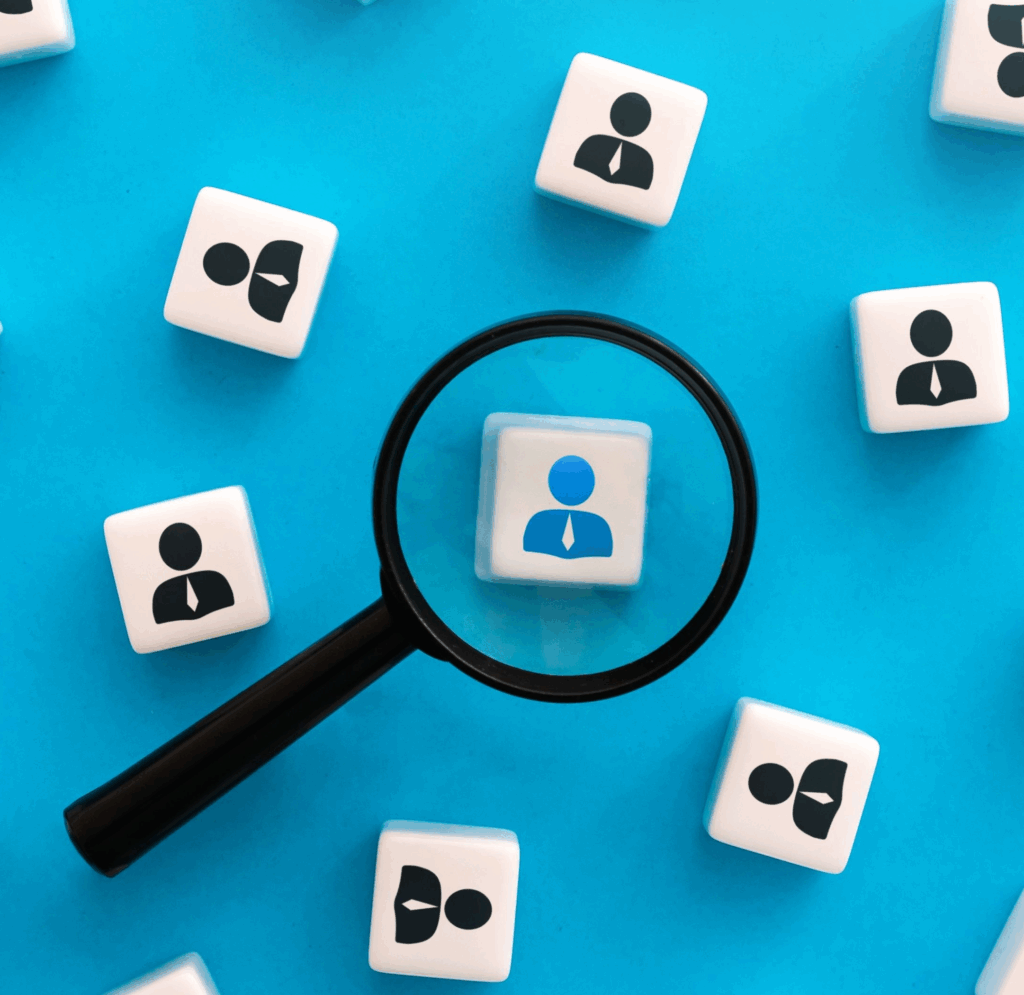 A series of dice on a blue background. They all have a silhouette of a person on them. The centermost one is blue instead of black and being viewed through a magnifying glass.