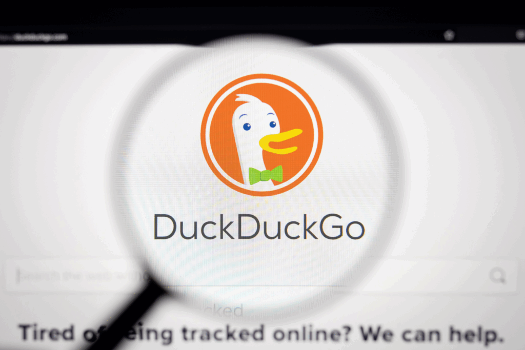 A magnifying glass is being held up to a computer monitor, bringing the DuckDuckGo logo and name into focus. On the bottom is says, "Tired of being tracked online? We can help."