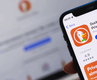 A cellphone has the DuckDuckGo app on the screen in front of a laptop with DuckDuckGo on it. It implies an answer to the questions, "Is DuckDuckGo safe?"