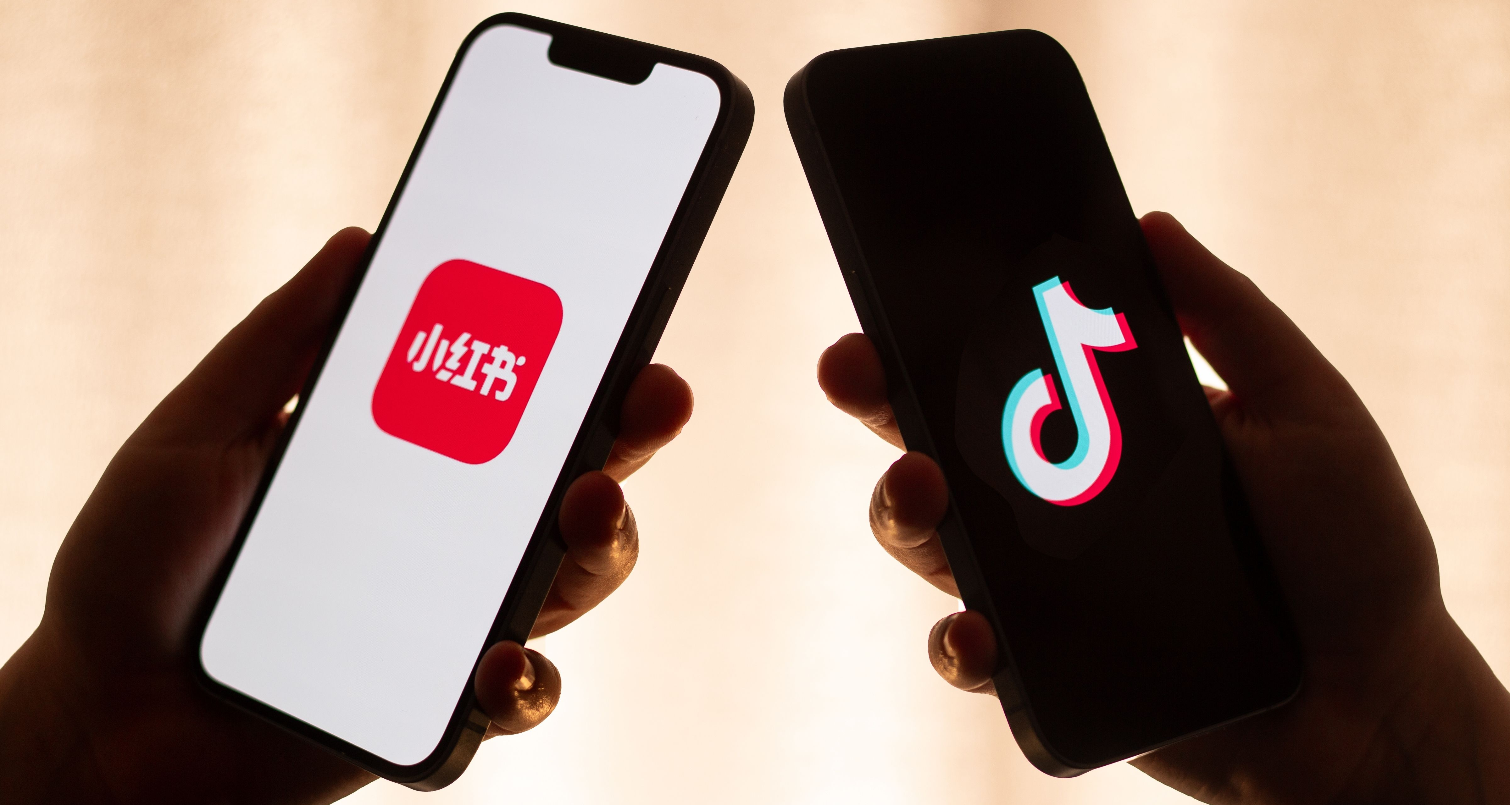 Two cellphones being held by hands that are in shadow. The left one has RedNote on it and the right one has TikTok.