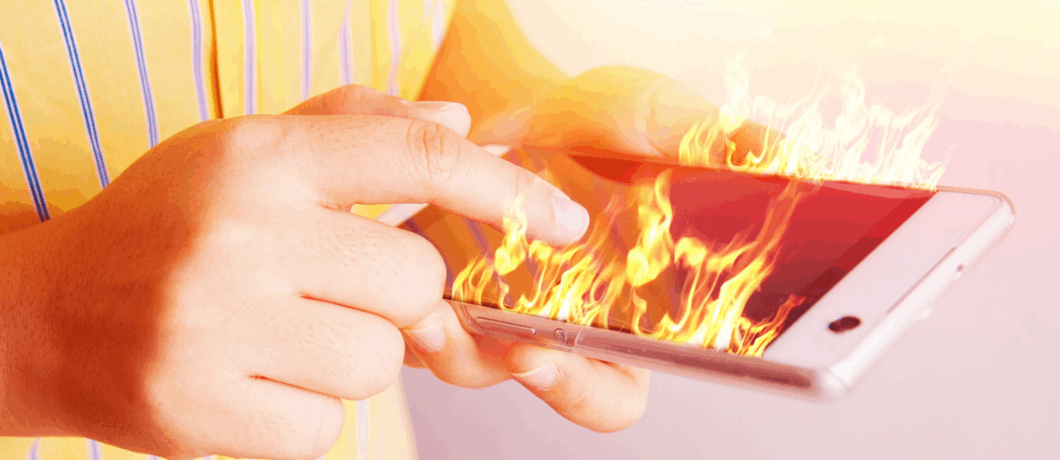 A person in a yellow shirt with blue stripes is holding a cellphone that is on fire.
