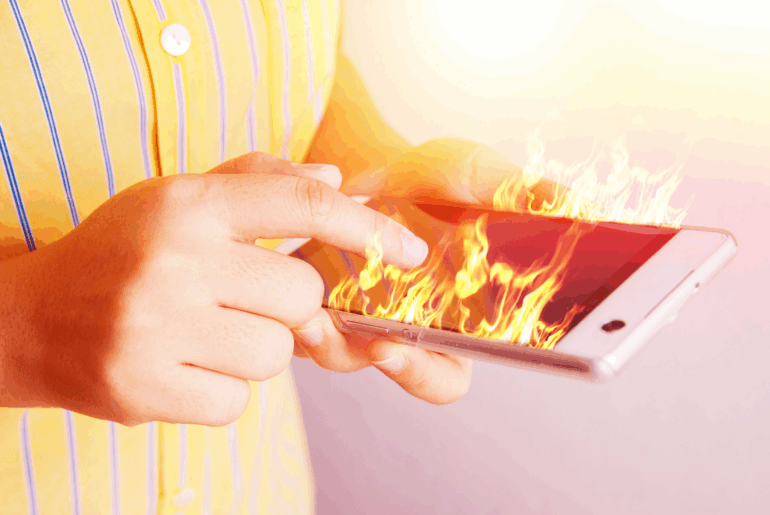 A person in a yellow shirt with blue stripes is holding a cellphone that is on fire.
