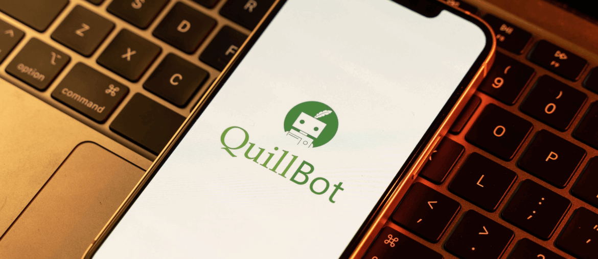 A cellphone sitting on top of a laptop keyboard. The QuillBot logo is on the screen.