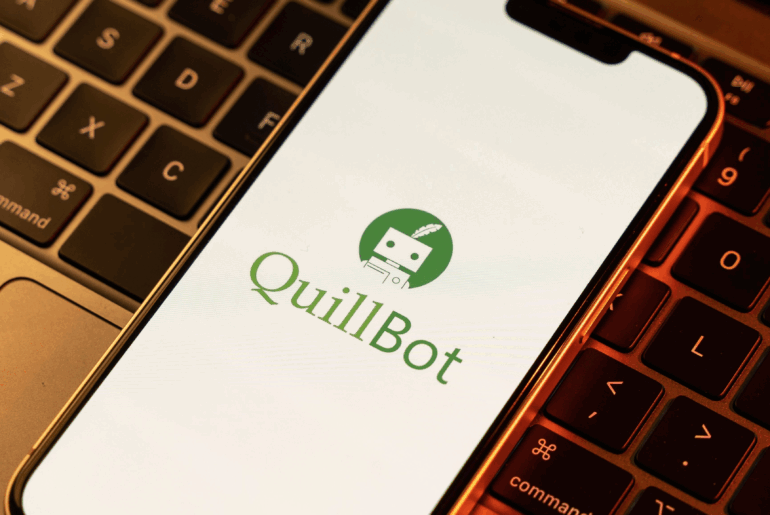 A cellphone sitting on top of a laptop keyboard. The QuillBot logo is on the screen.