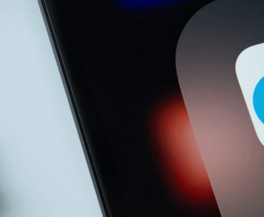 A closeup of a phone with the OnlyFans app icon showing on it and an earbud on the table under it.