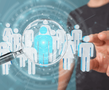 A man in a black t-shirt is reaching out toward the screen. There are several icons of people hovering in front of him. One of the icons is blue and being looked at through a magnifying glass.